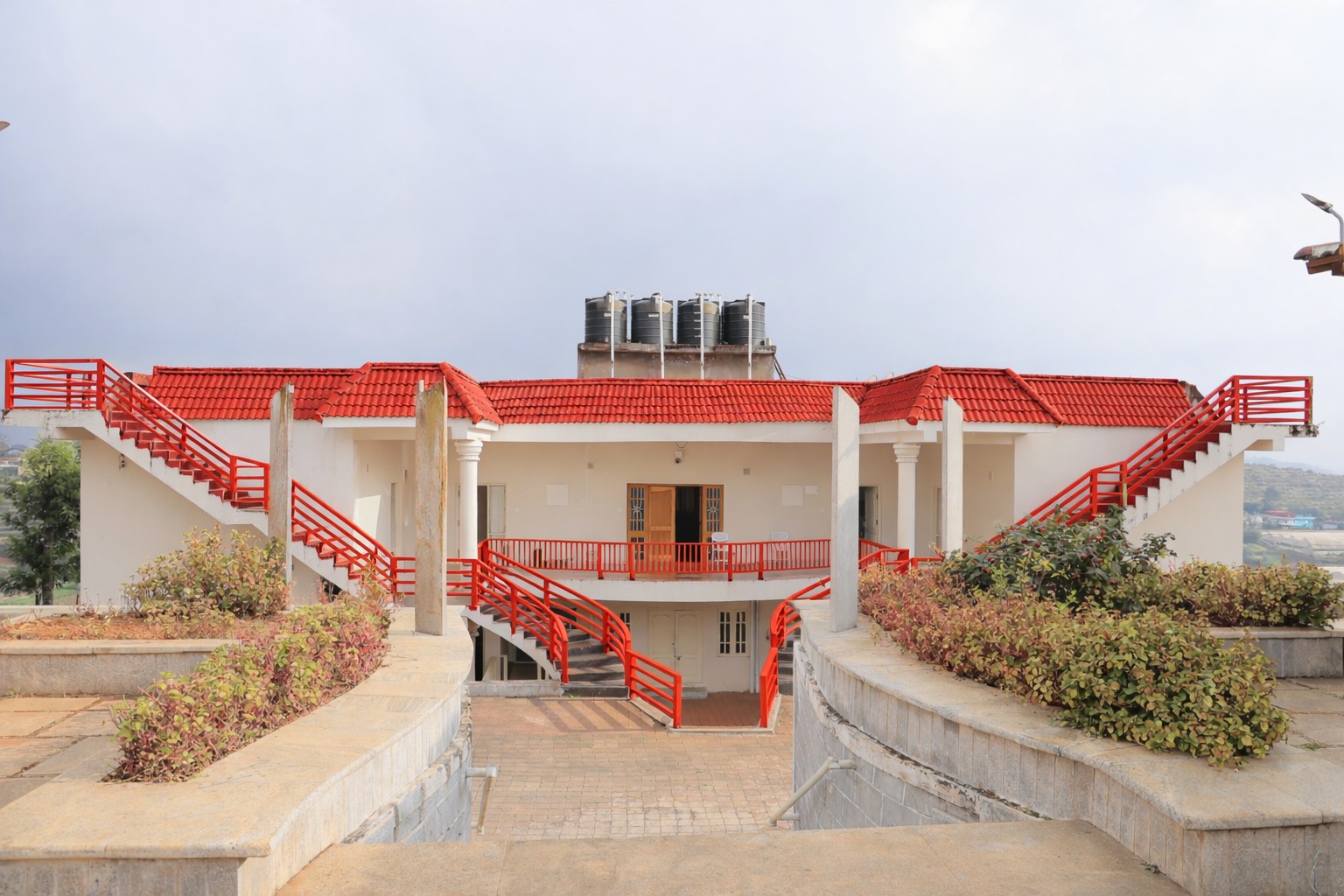 Modern luxury resort building with red roof, grand entrance, landscaped pathways, and spacious outdoor area 