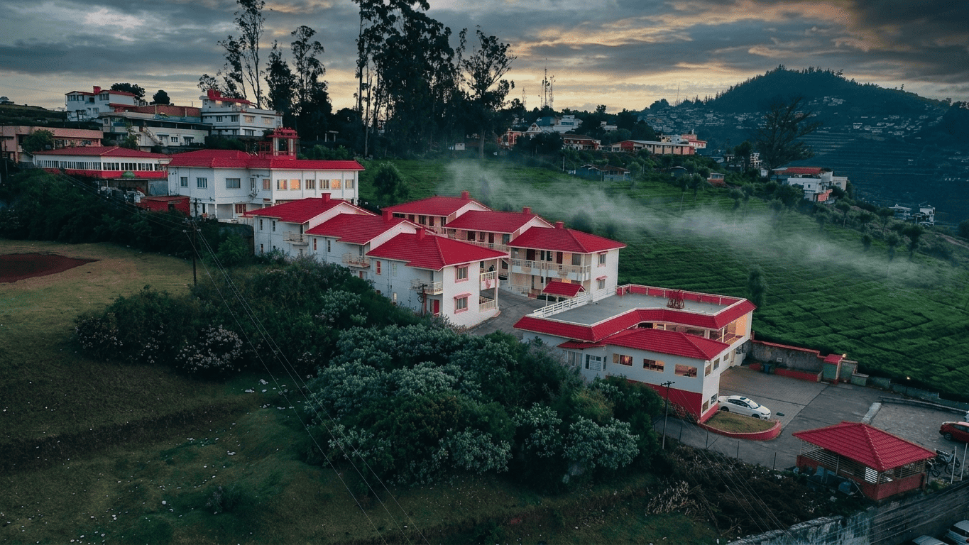 Drone view of a luxury hillside resort surrounded by lush tea plantations, misty mountains, and scenic landscapes.
